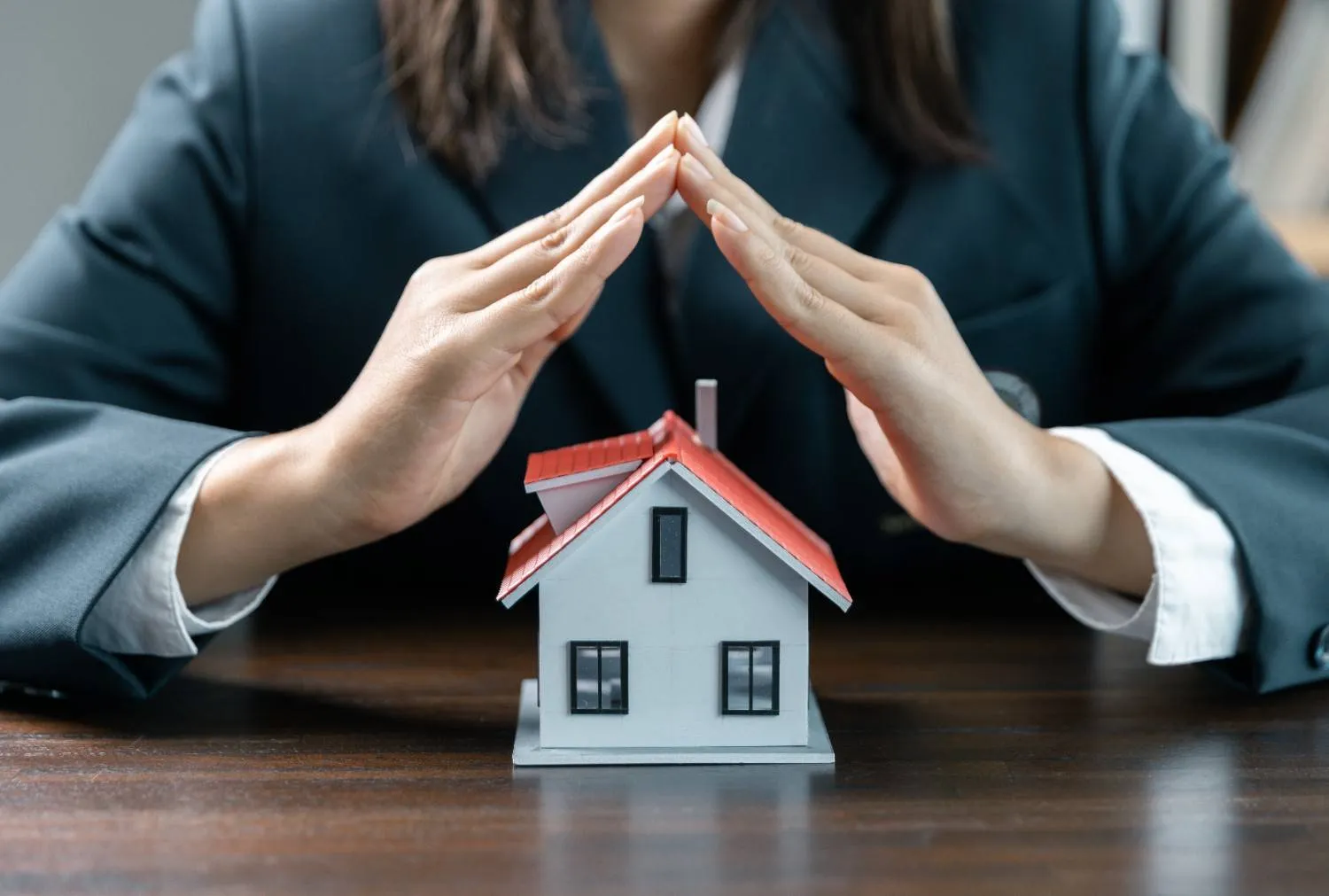 Hands sheltering a small model house